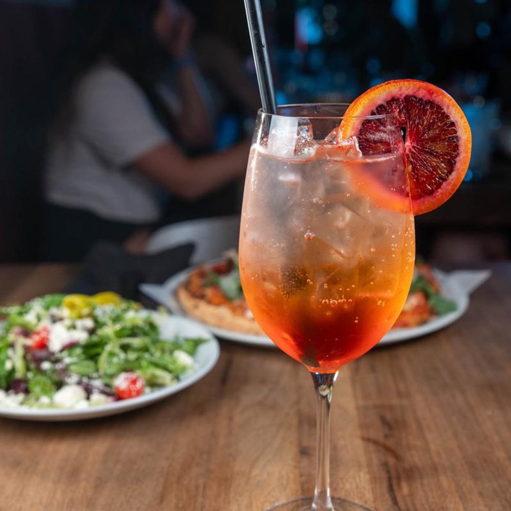 Aperol Spritz Cocktail On A Table With Food In The Background.