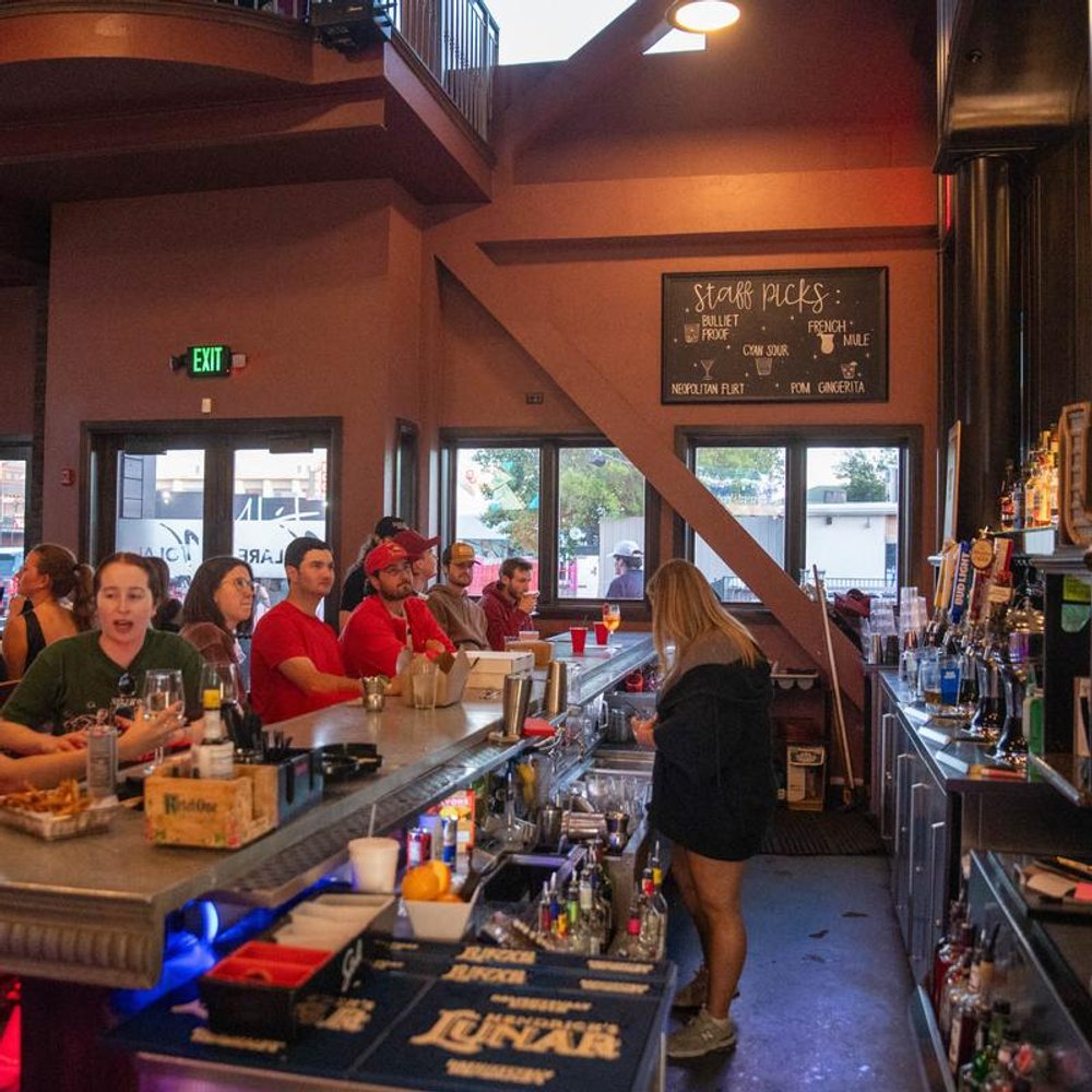 Bar Interior With A Bartender Serving Customers That Are Seated At A Bar Counter.