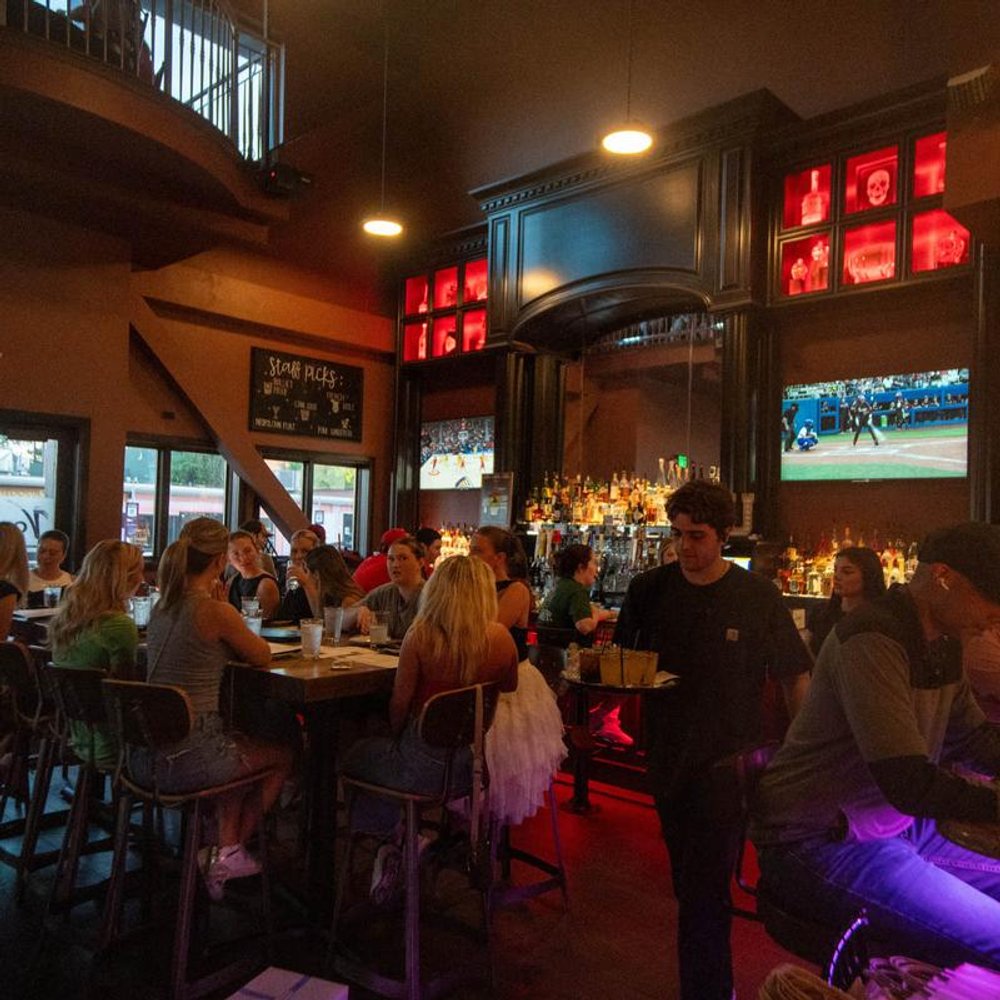 Bar Interior With Guests Seated At Tables Servers And Tvs Playing Sports.