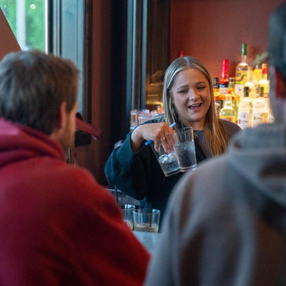 Bartender Interacting With Customers Holding Glasses Of Iced Water.