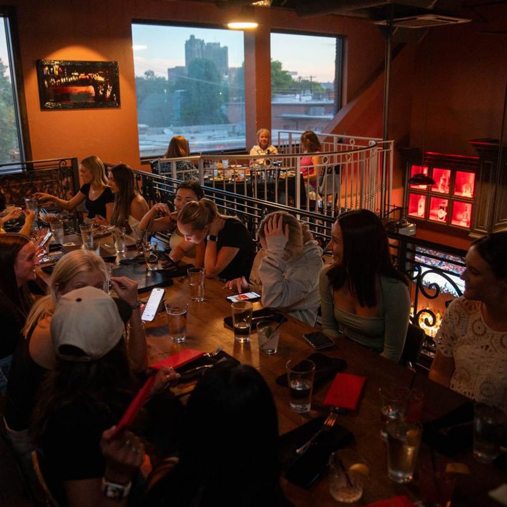 Big Group Sitting At A Table On The Mezzanine Facing Large Window And Wall Art.