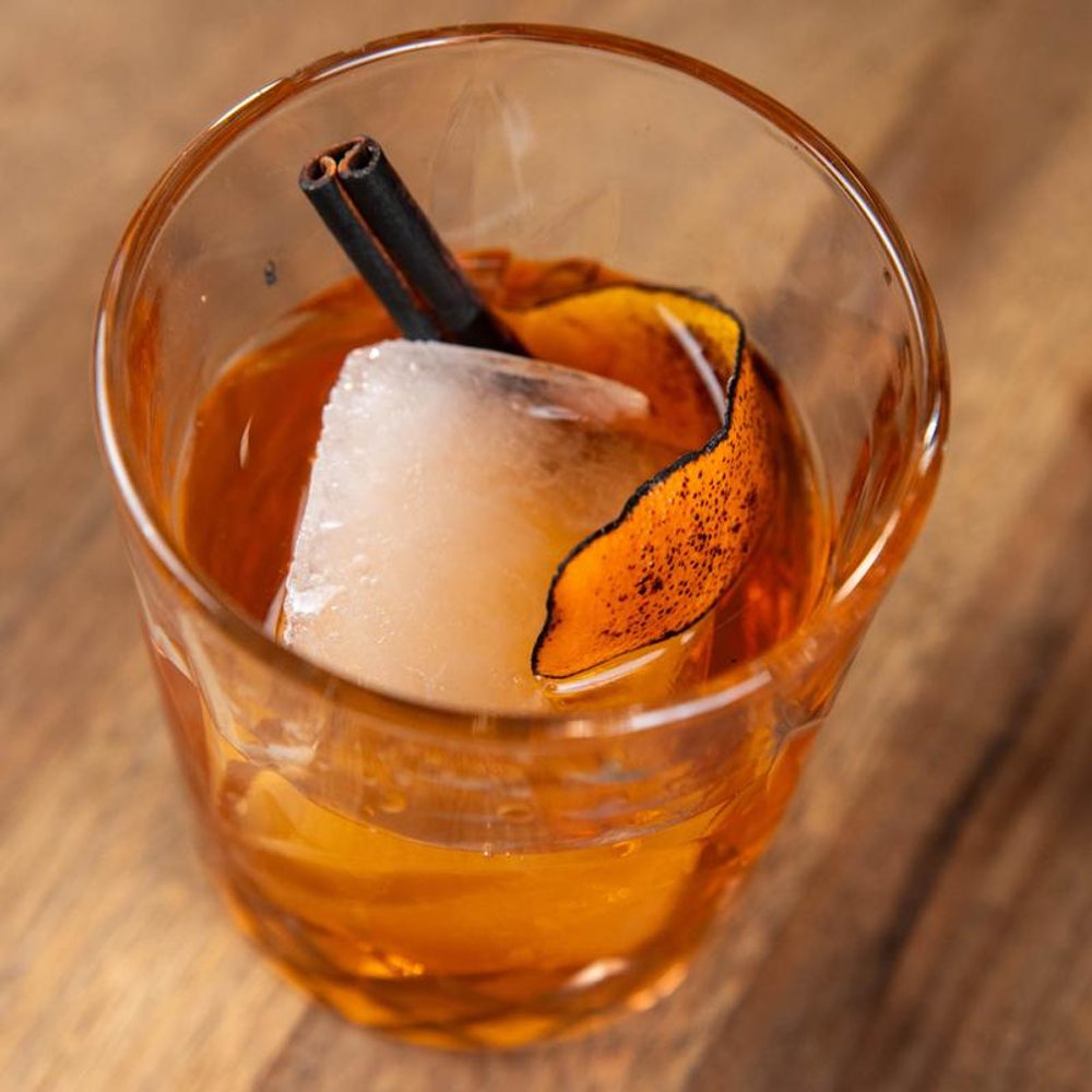 Bulleit Proof In A Rocks Glass With One Ice Cube And A Burnt Orange Peel.