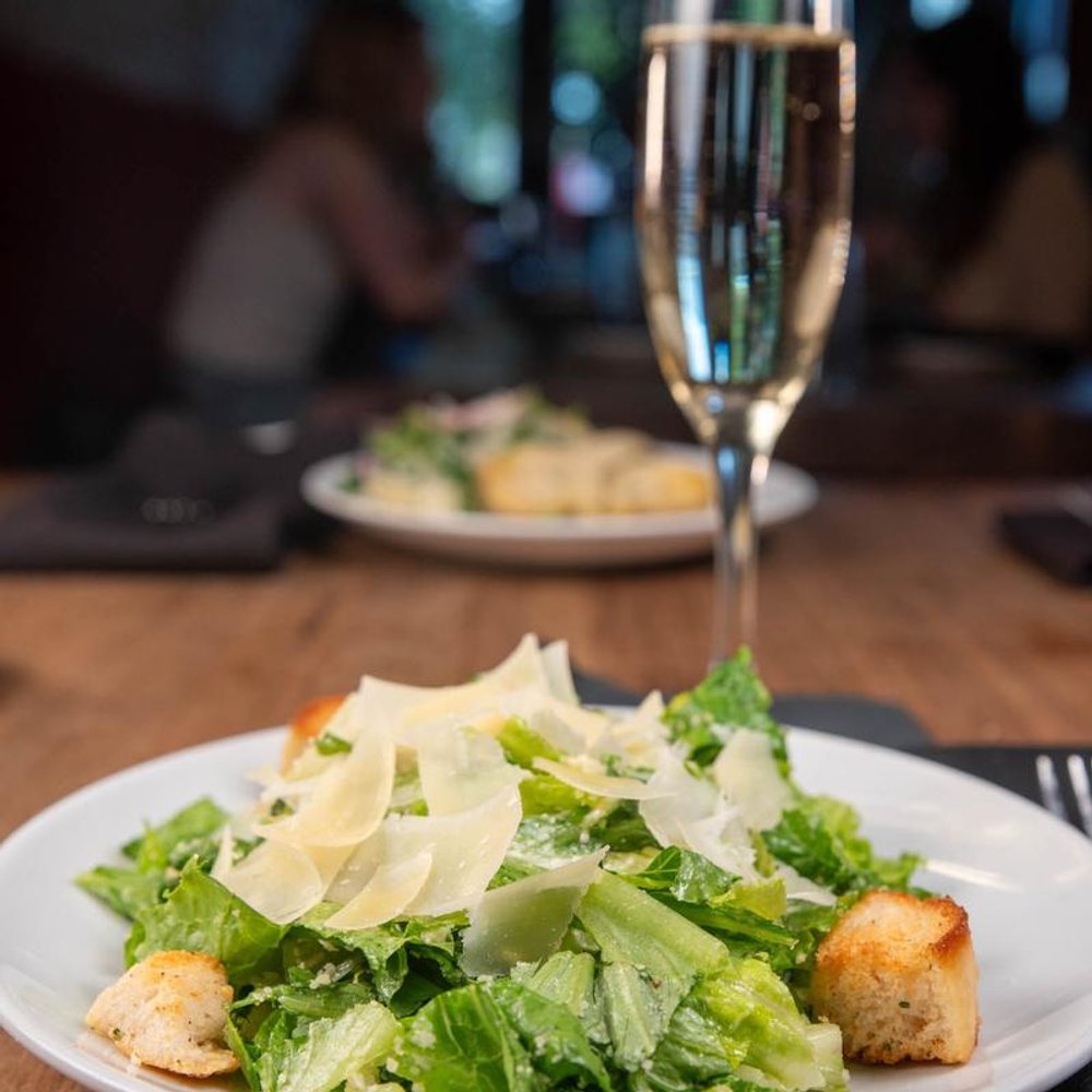 Caesar Salad Served With A Glass Of Sparkling Wine Other Dish In The Background.