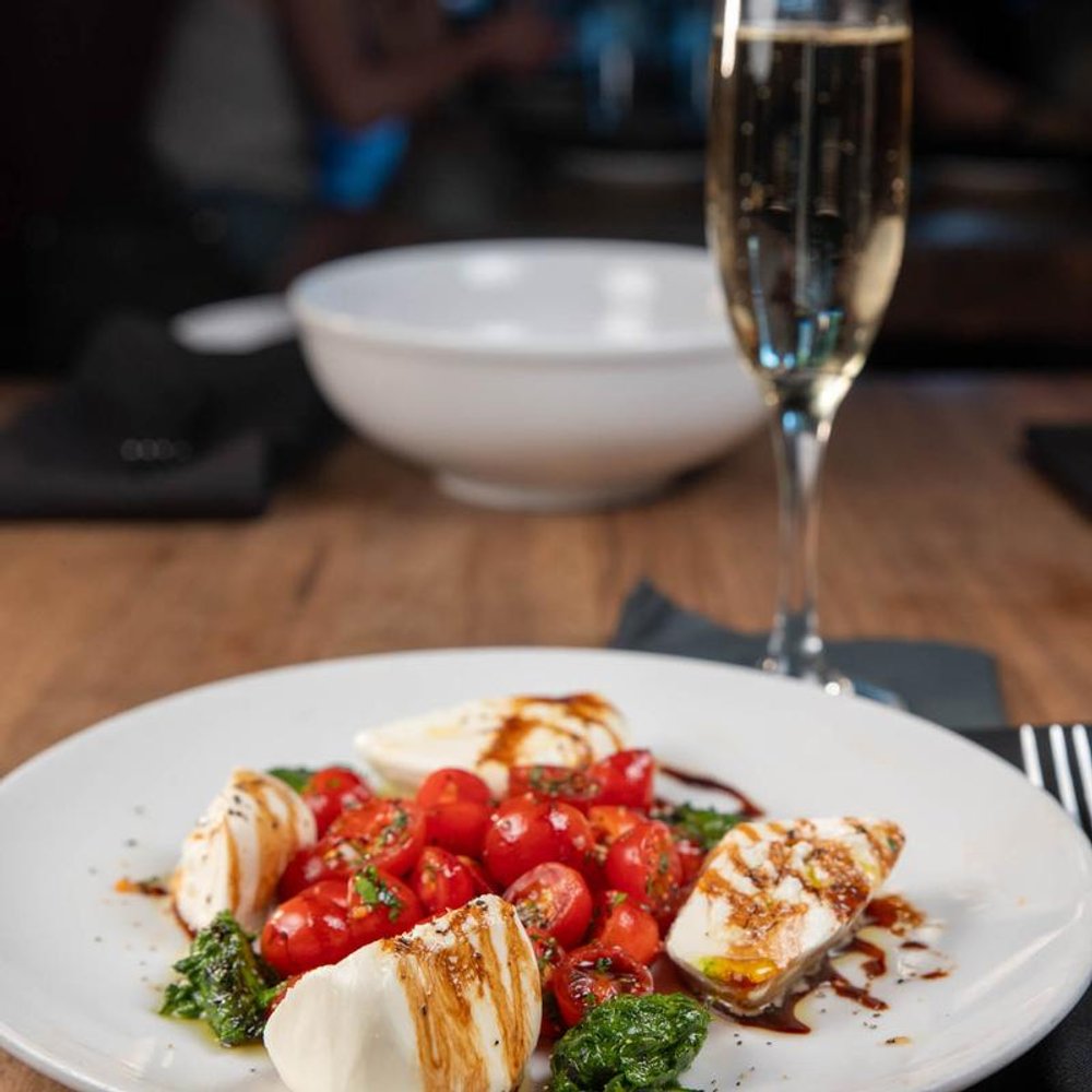 Caprese Salad With Burrata Tomatoes And Basil Beside A Glass Of Champagne.