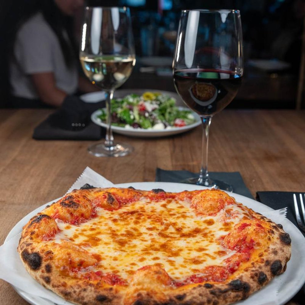 Cheese Pizza On A Table With Glasses Of Wine And A Salad In The Background.