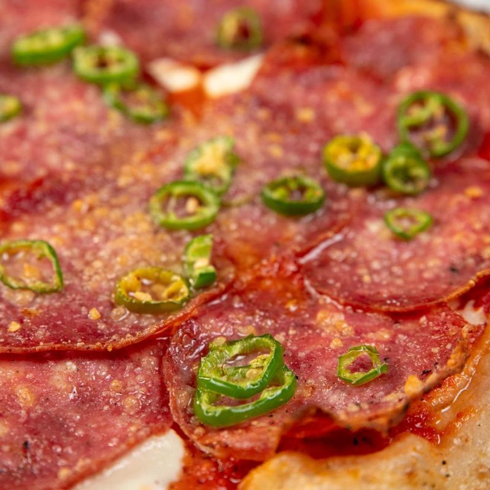 Close Up Of A Soppressata Pizza With Red Sauce And Serrano Peppers.