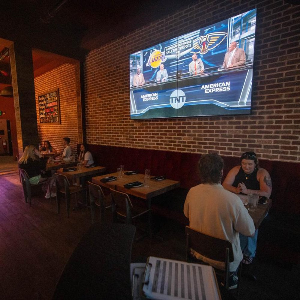 Dimly Lit Bar With Guests Seated At Tables And A Big Tv.