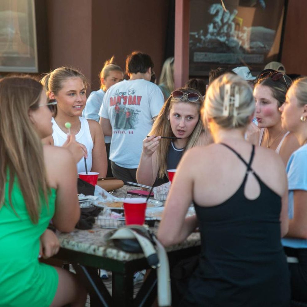 Group Of People Eating And Drinking At An Outdoor Table On A Sunny Day.