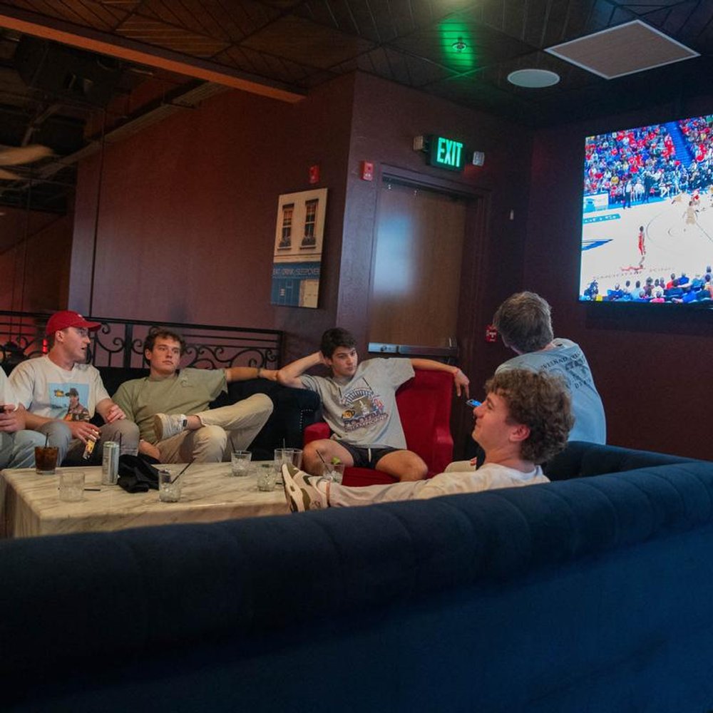 Group Of People Relaxing On A Sofa Watching A Basketball Game On A Tv.