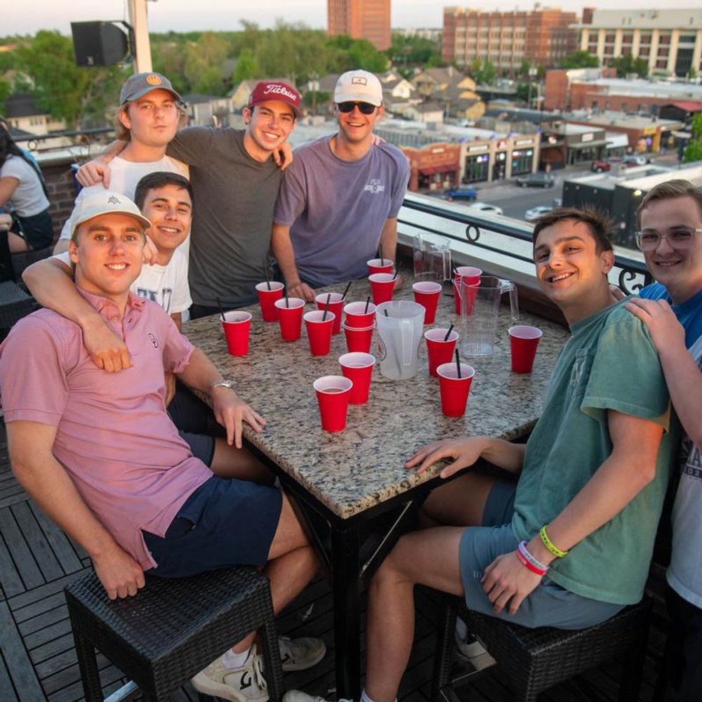 Group Of People Sitting At A Table On A Rooftop Posing For A Photo.