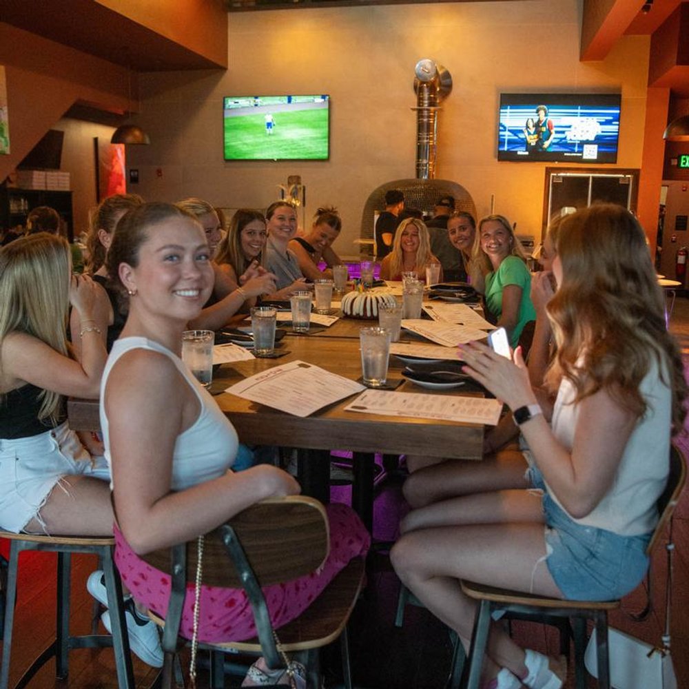 Group Of People Sitting At The Big Table With Menus Tvs In The Background.