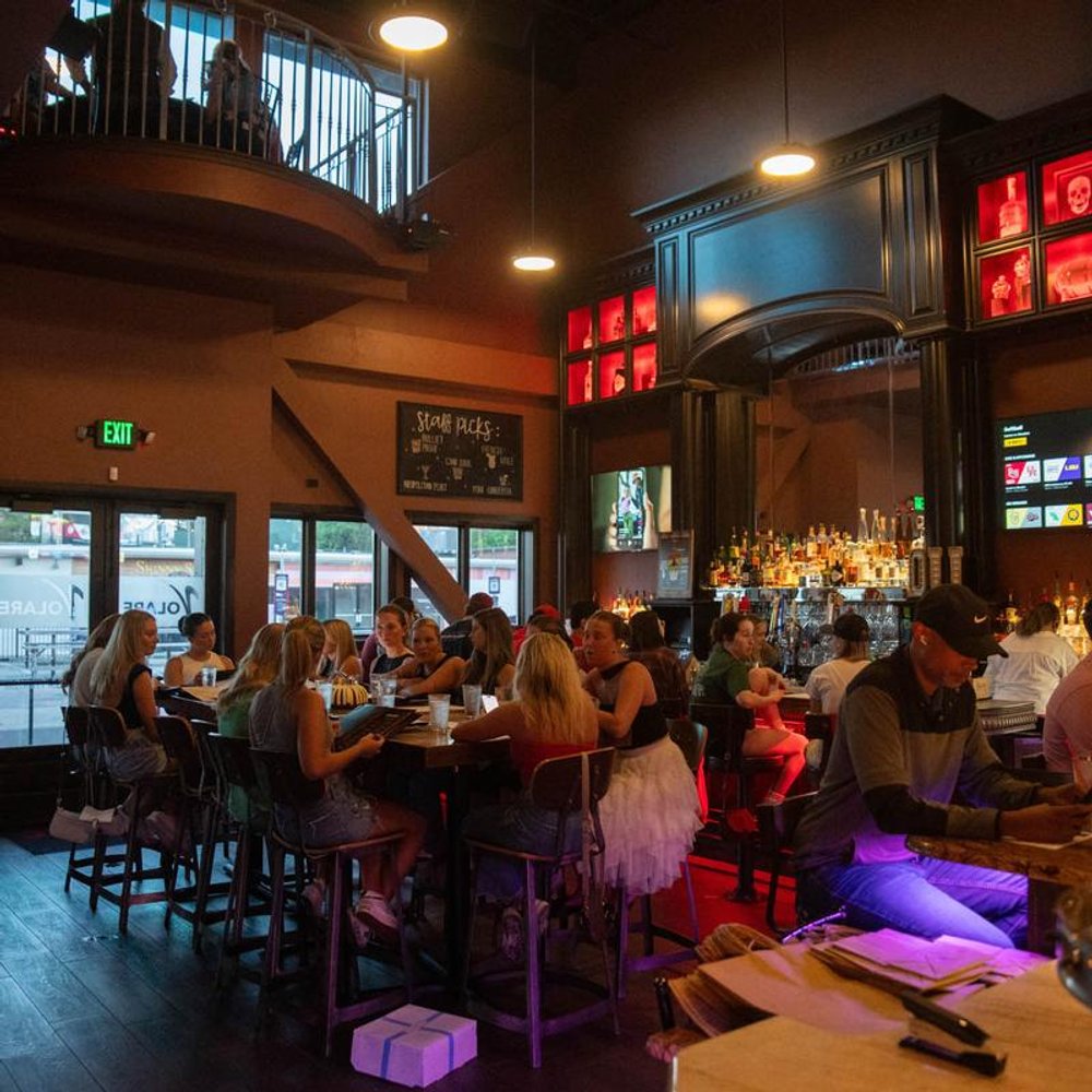 Guests Dining And Socializing In A Dimly Lit Bar With A Mezzanine.