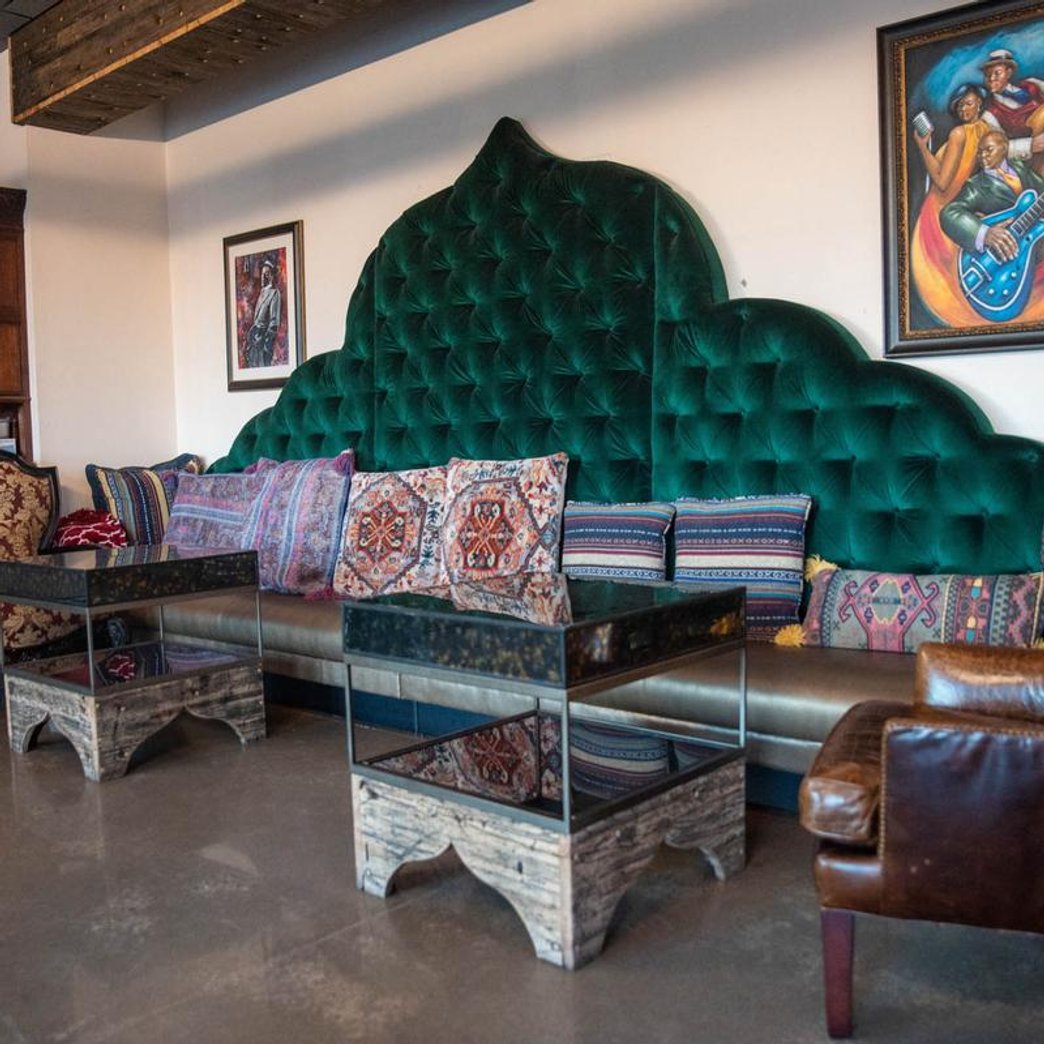 Interior featuring a green couch with pillows tables armchairs and wall art