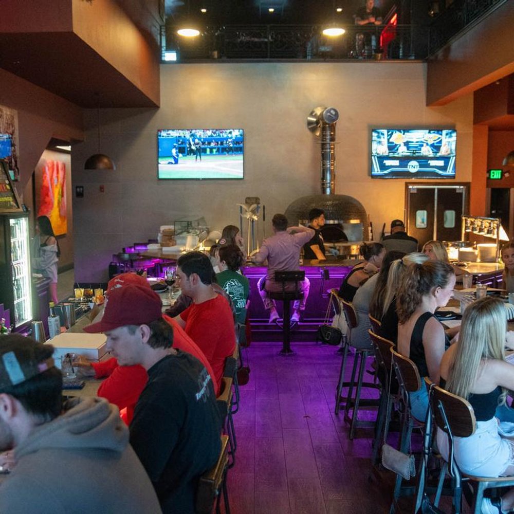 Interior Of A Busy Pizza Bar With An Open Pizza Kitchen Guests At Tables.