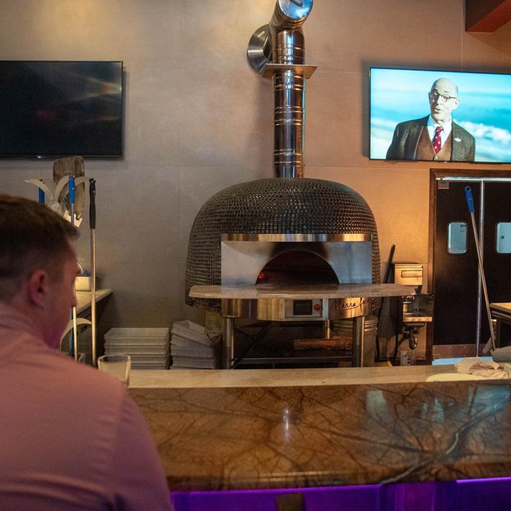 Interior With A Wood Fired Oven And A Person Sitting At A Counter.