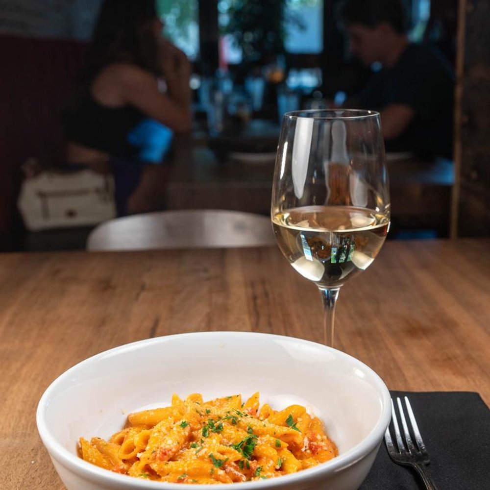 Penne Vodka And A Glass Of Wine On A Table People In The Background.