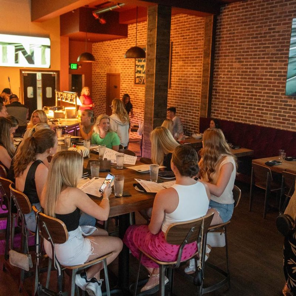People Seated At Tables In A Dimly Lit Restaurant With Brick Walls.