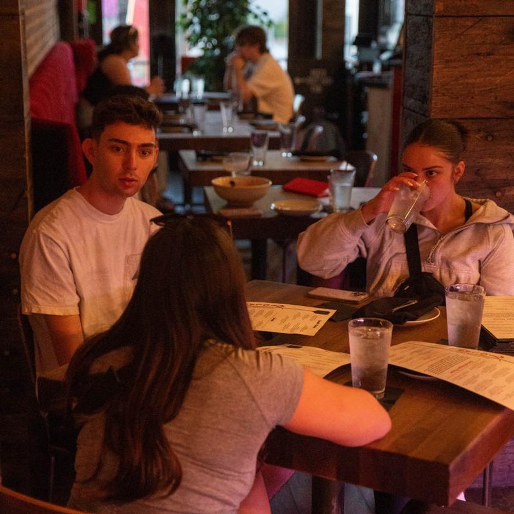 People Seated At Tables In A Dimly Lit Restaurant With Menus.