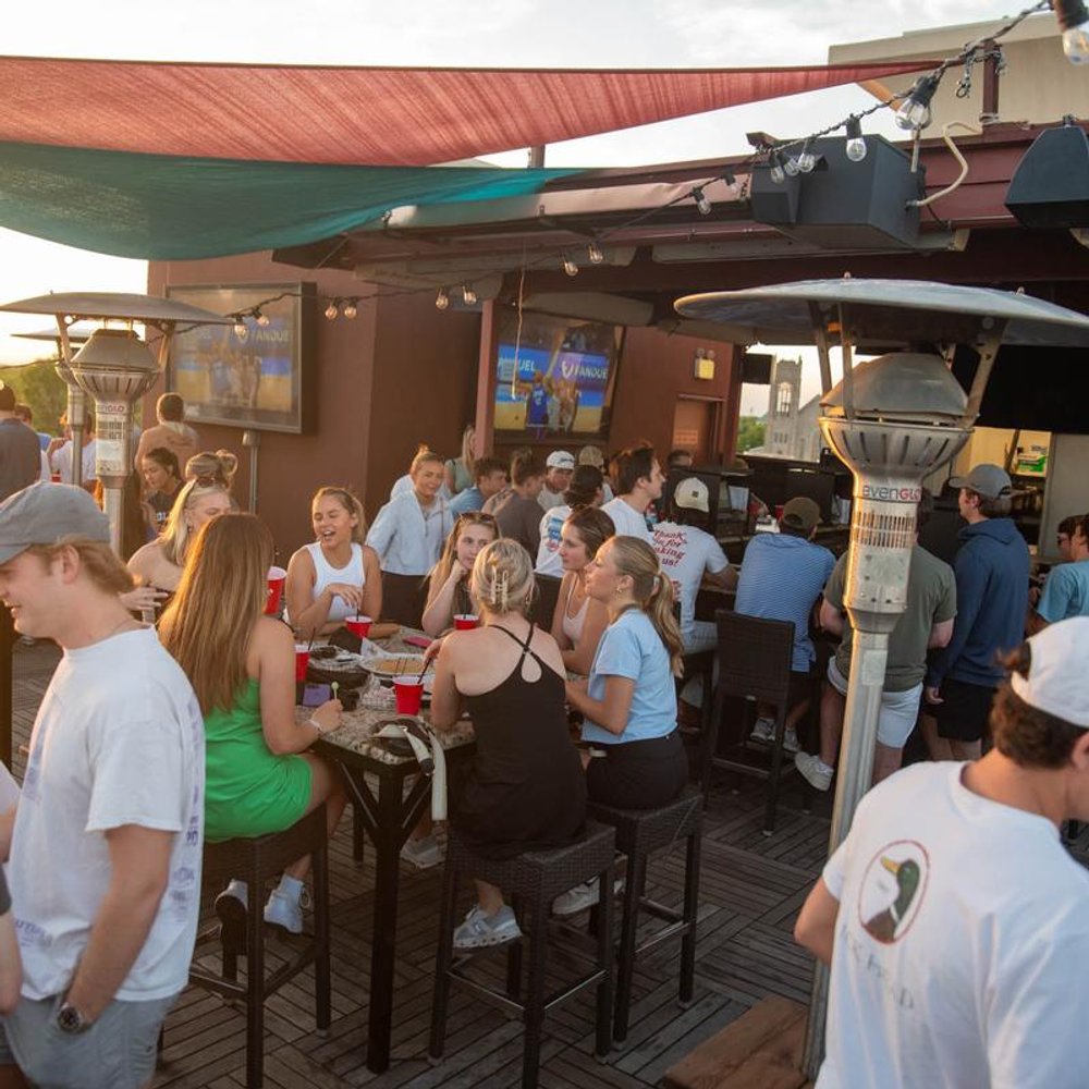 People Socializing On A Bar Terrace With Sun Shades String Lights And Heaters.