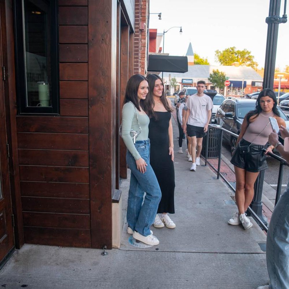 People Standing Outside A Building On A Sidewalk.