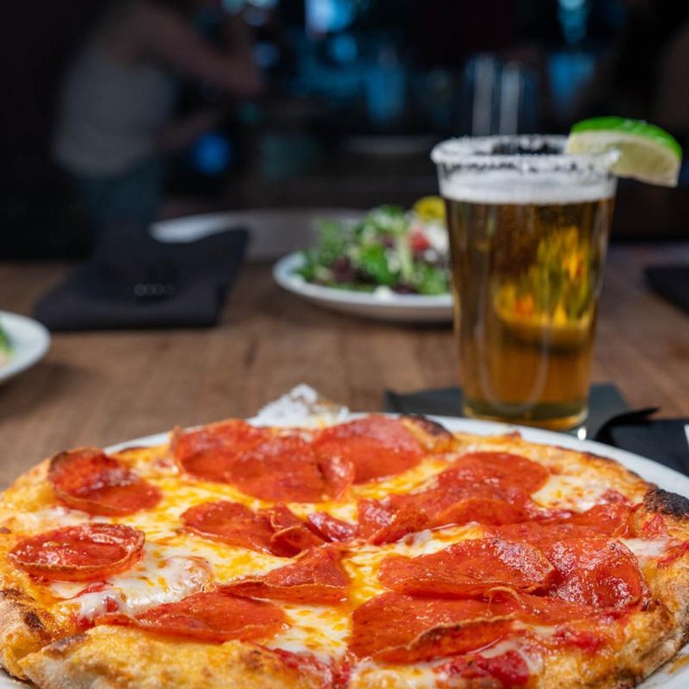 Pepperoni Pizza In The Foreground With A Beer And A Salad In The Background.