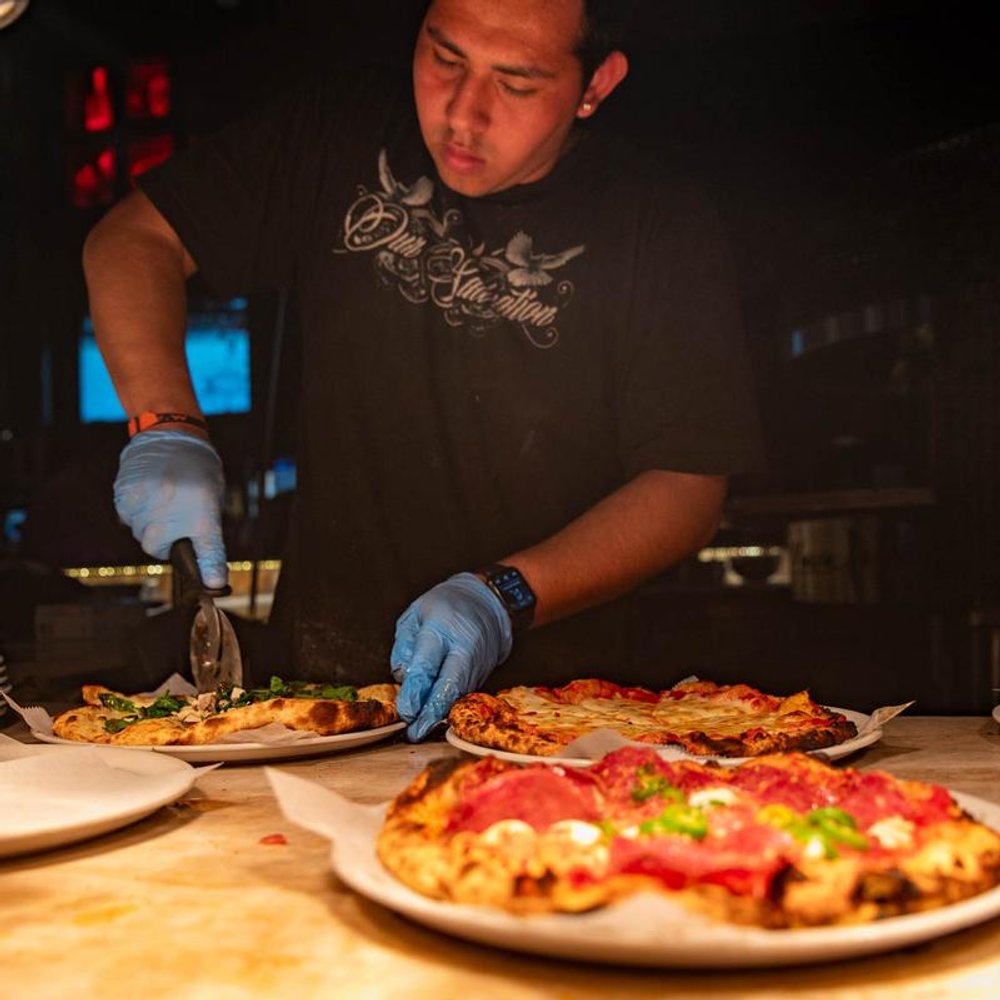 Person In Gloves Cutting Pizzas On A Counter.
