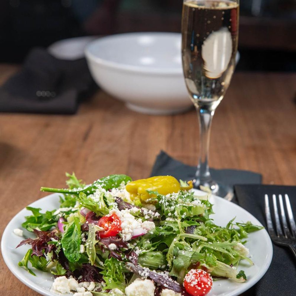Salad With Mixed Greens Tomatoes Feta And Olives Alongside Sparkling Wine.