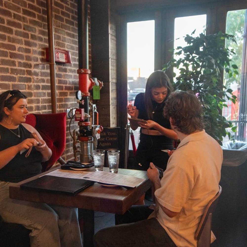 Server Taking Orders From A Table By The Windows And Plants.
