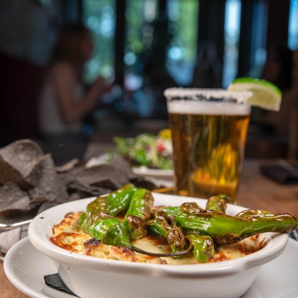Shishito Peppers Over Jalapeno Artichoke Dip Other Food And A Beer In The Background.
