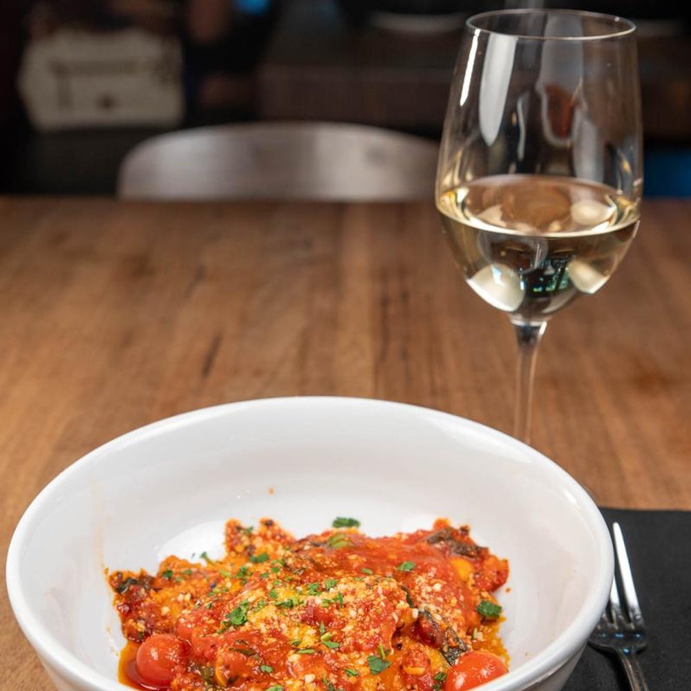 Short Rib Ravioli Next To A Glass Of White Wine On A Table.
