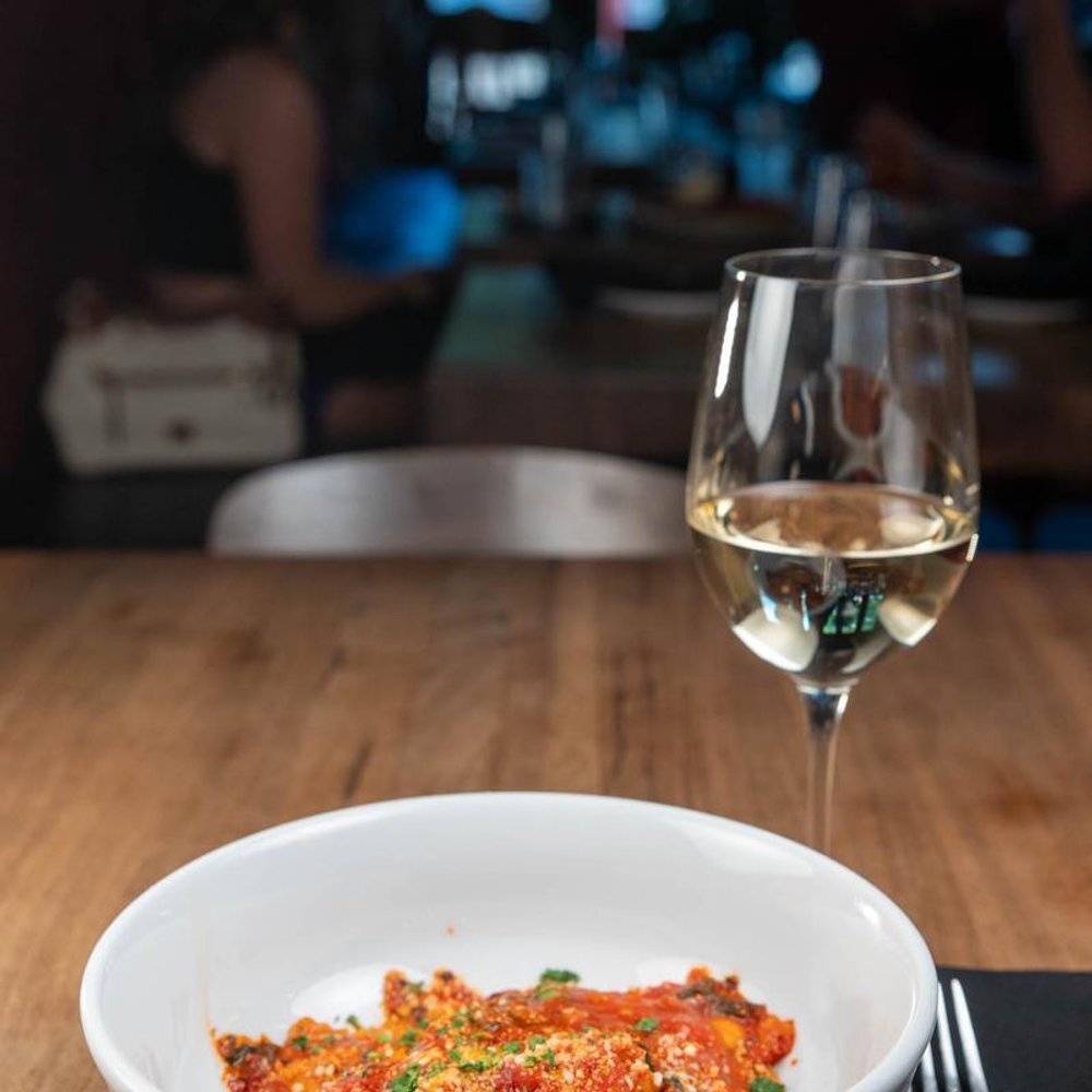 Short Rib Ravioli Served With A Glass Of White Wine On A Table.