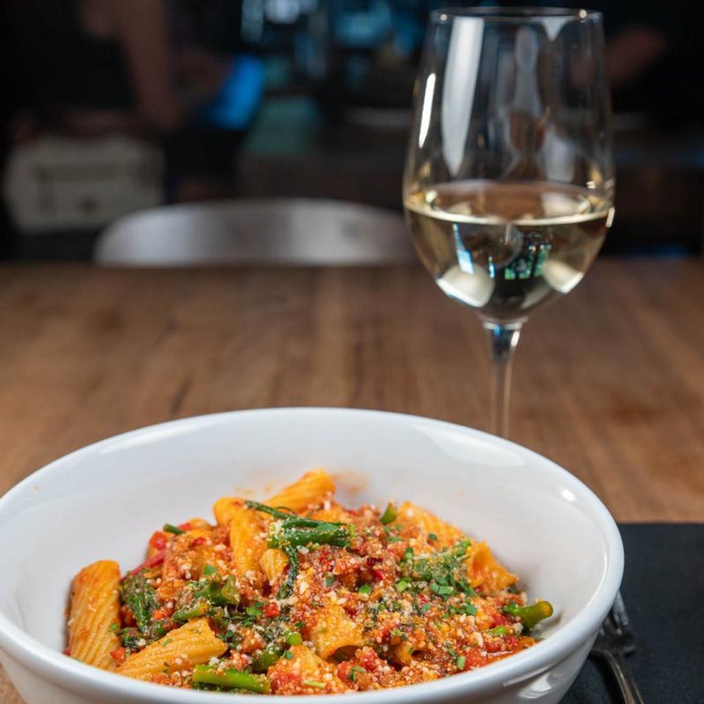 Spicy Rigatoni Served With A Glass Of White Wine On A Table.