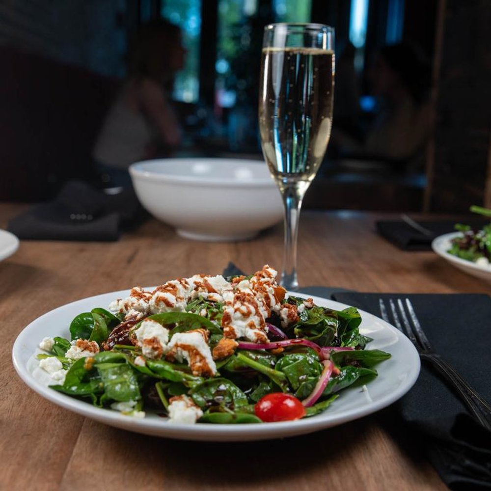 Spinach Salad With A Glass Of Sparkling Wine And Another Dish In The Background.