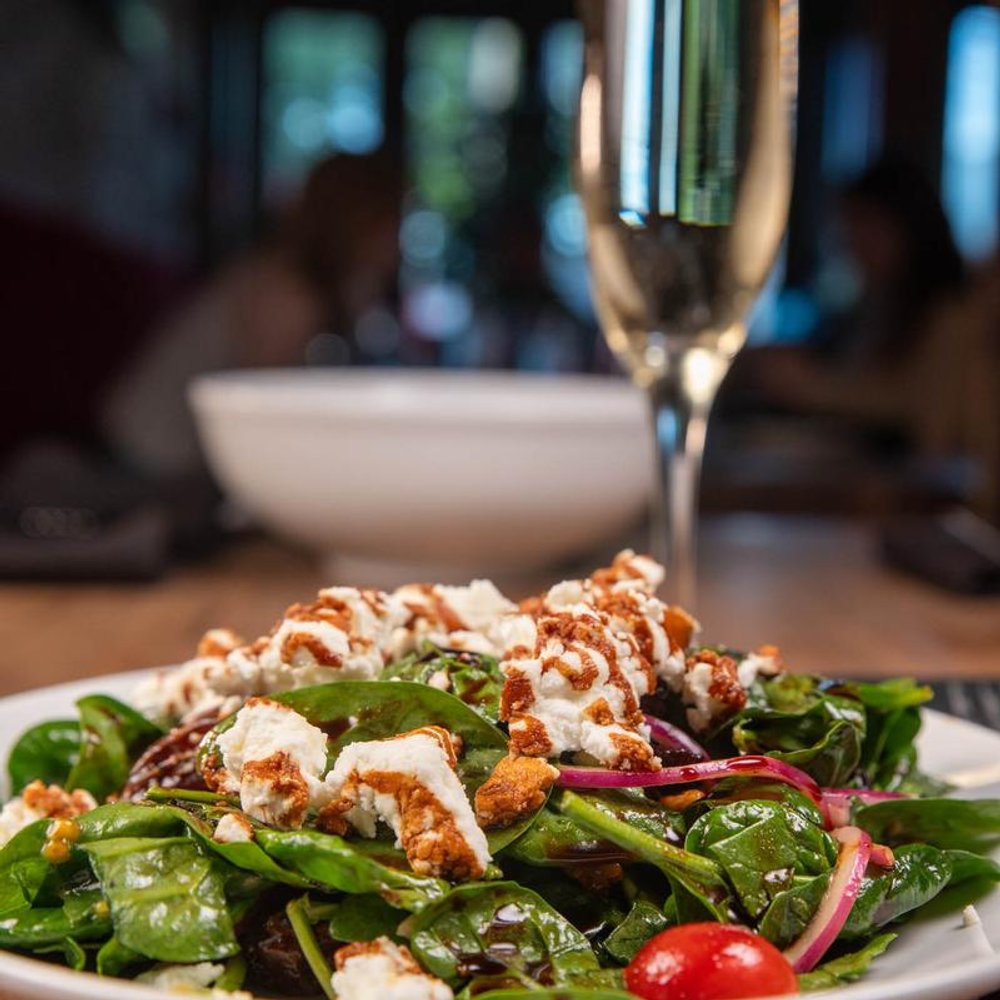 Spinach Salad With Cheese And Tomatoes And A Glass Of Champagne In The Background.