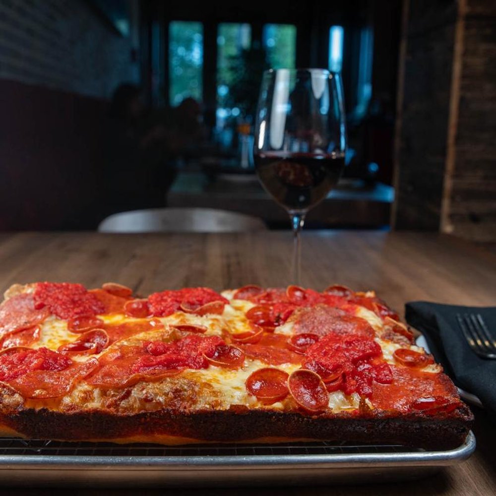 Square Pepperoni Pizza With Red Wine On A Table Guests In The Background.