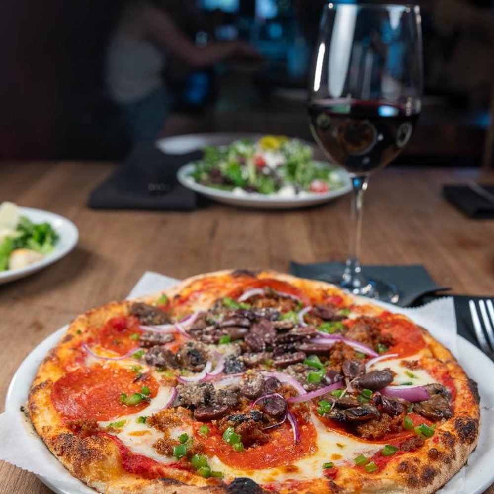 Supreme Pizza With Red Wine On A Table Salads In The Background.
