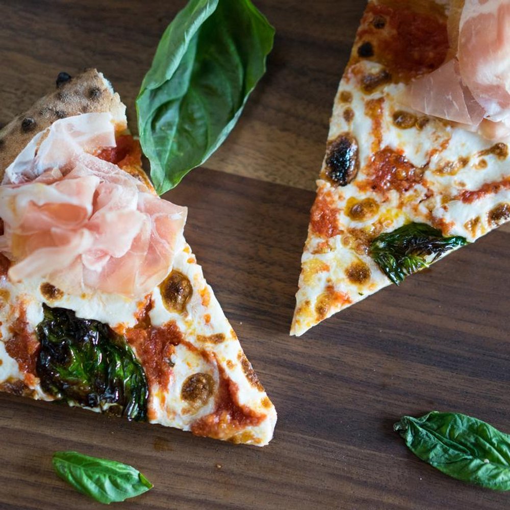 Two Slices Of Pizza On A Table Basil Leaves Beside Them.