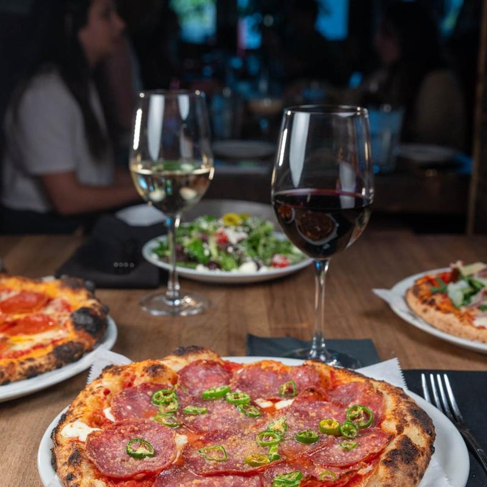 Various Pizzas And Glasses Of Wine On A Table.