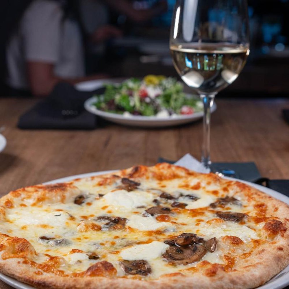 White Truffle Pizza With A Glass Of White Wine And A Salad In The Background.