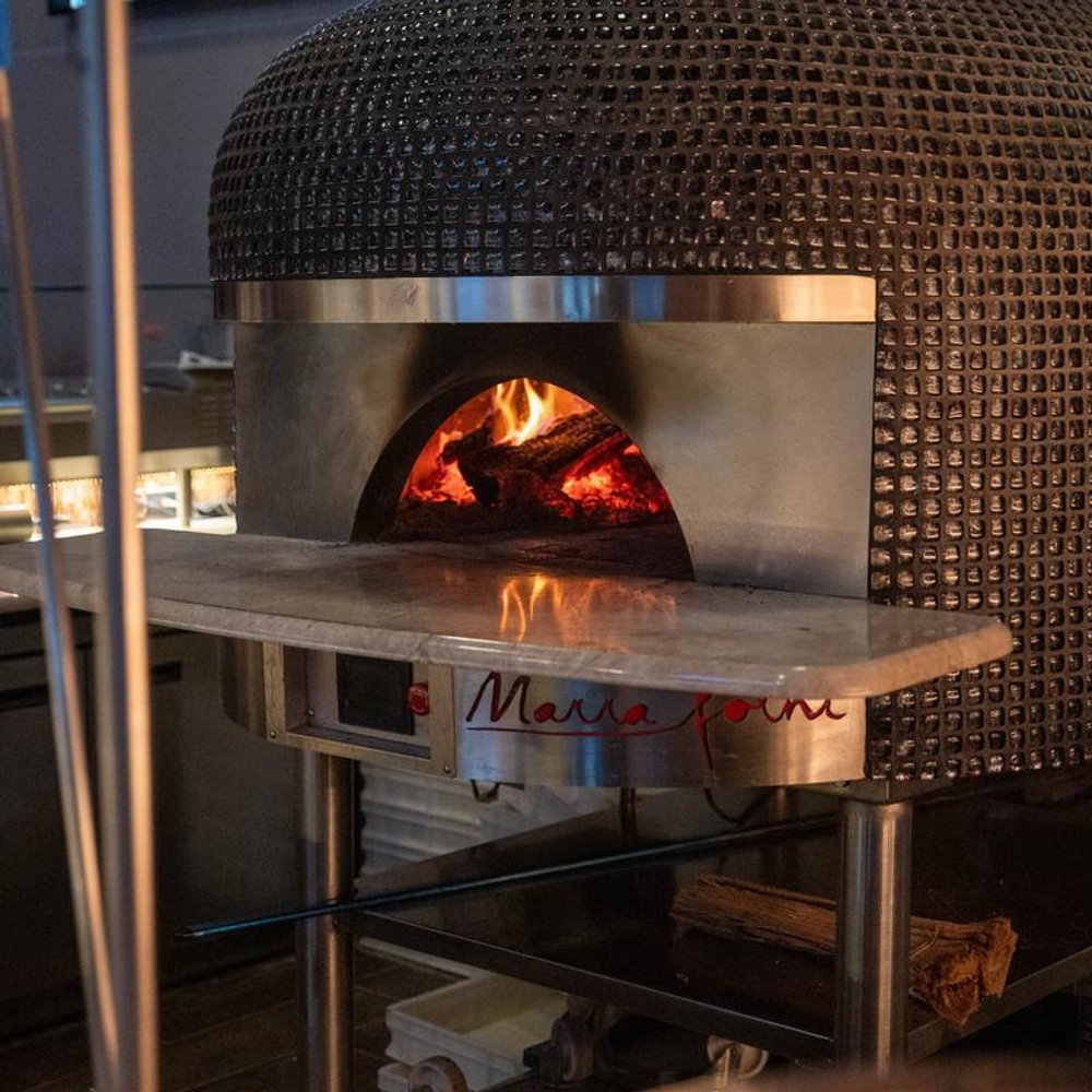 Wood Fired Pizza Oven With Visible Flames In A Restaurant Kitchen Setting.